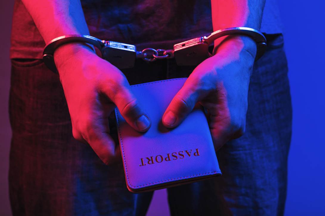 A person in handcuffs holds a passport in a dramatic red and blue light. The image is a header to legal content about false imprisonment, passport in hand.